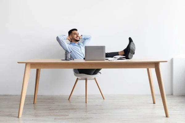 Leende arabisk man lutar sig tillbaka sitter vid skrivbordet — Stockfoto