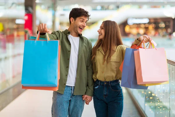 Pareja emocionada mostrando coloridas bolsas de compras en el centro comercial —  Fotos de Stock