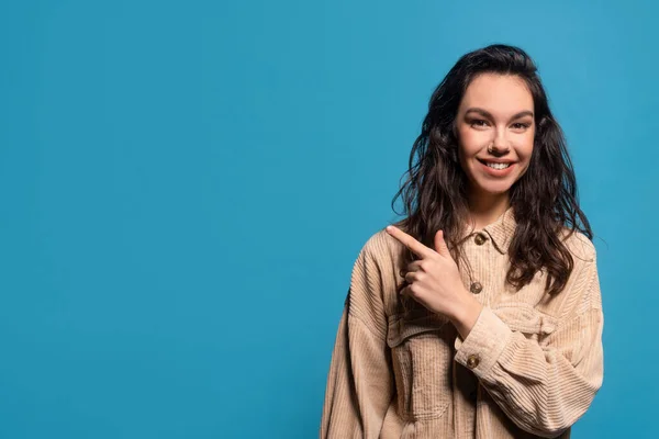 Smiling young european brunette female in casual pointing finger at empty space — Φωτογραφία Αρχείου