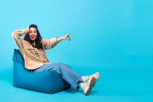 Glad surprised young european brunette lady with open mouth presses her hand to head sits on bagchair — Stockfoto