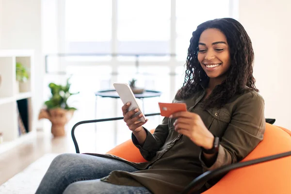 Smiling black lady using phone and credit card at home — Foto Stock