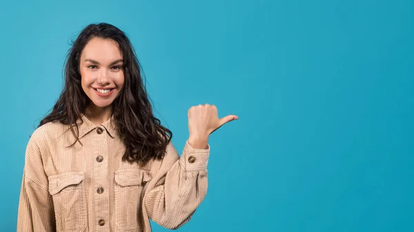 Glimlachen jong europees brunette dame in casual wijzend vinger naar lege ruimte geïsoleerd op blauwe achtergrond — Stockfoto