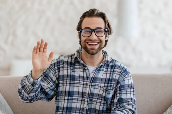 Souriant millénial caucasien mâle enseignant avec chaume dans des lunettes agitant la main à la caméra dans le salon — Photo