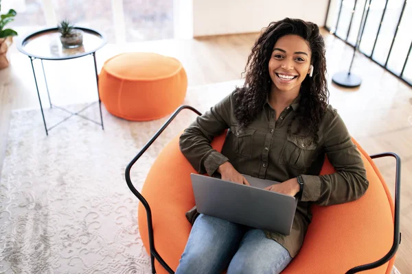 Portrait of smiling black woman in earbuds using laptop