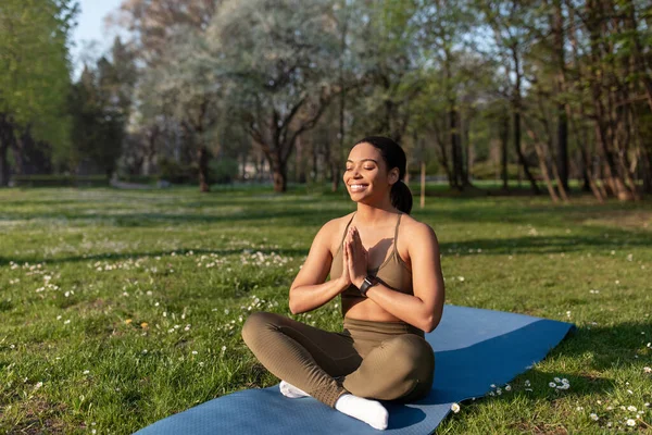 Full length of young black woman meditating with closed eyes, making namaste gesture at city park, copy space — стоковое фото