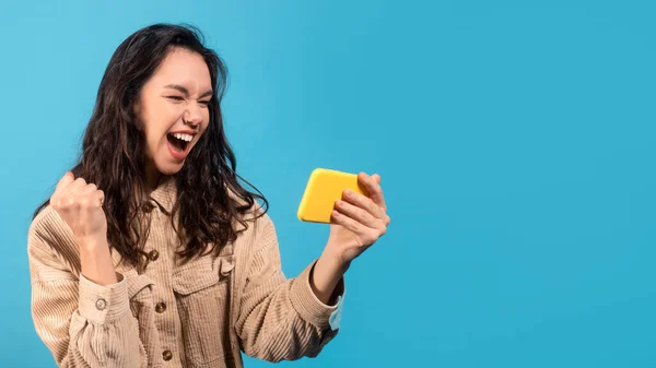 Felice felice giovane donna bruna europea in casual guardando smartphone e fare gesto vincente — Foto Stock