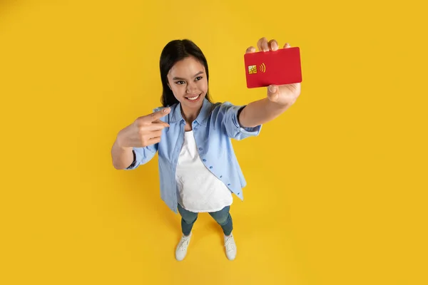 Glückliche ziemlich lustige junge Japanerin in lässiger Weise zeigt mit dem Finger auf Kreditkarte mit Leerzeichen — Stockfoto