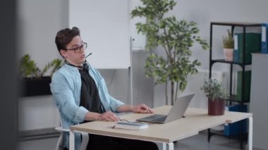 Distant work. Young guy helpline operator ending call with client, taking off headset at looking at window at office