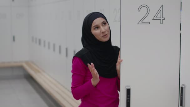 Young middle eastern woman wearing hijab talking with interlocutor, standing at modern locker room at gym, free space — Stok video