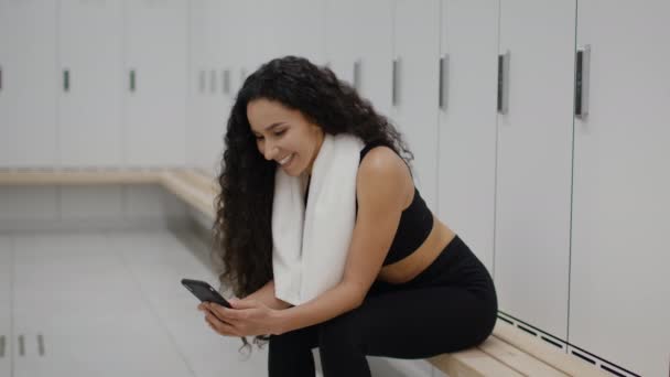 Молодая спортивная женщина веб-серфинг онлайн в социальных сетях на смартфоне, отдых в раздевалке спортзал после фитнес-тренировки — стоковое видео