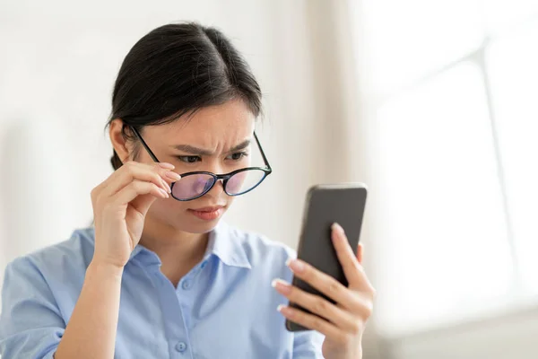 Confused asian woman holding smartphone, removing eyeglasses — Stok fotoğraf