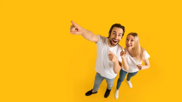 Glad surprised excited millennial caucasian husband and wife in white t-shirts pointing up at empty space — Foto de Stock