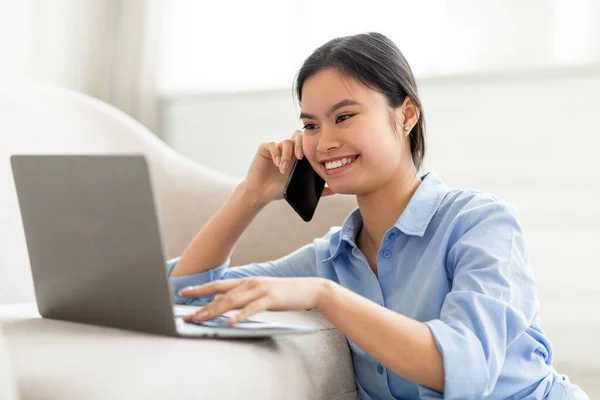 Closeup of smiling chinese lady talking on phone, using laptop — Stockfoto