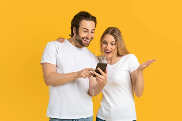 Fröhlicher Millennial-Mann in weißem T-Shirt zeigt seiner überraschten Frau Telefon — Stockfoto