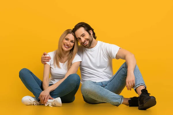 Cheerful young attractive european man with beard and female hugging, sit on floor, isolated on yellow background — Stok fotoğraf