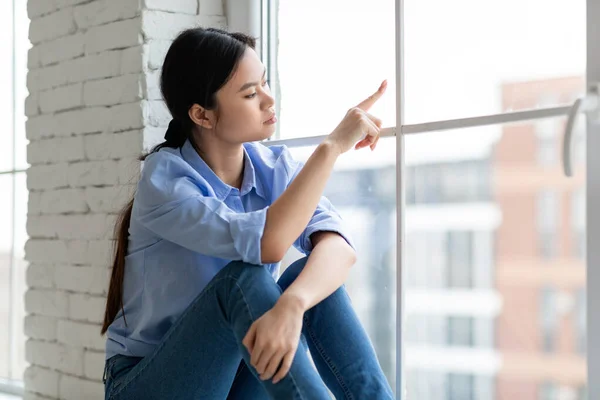 Upset millennial asian woman sitting on window at home — Photo