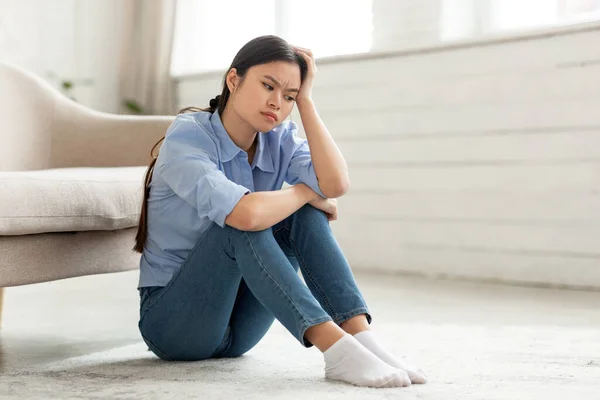 Frustrated korean woman sitting on floor at home — стокове фото