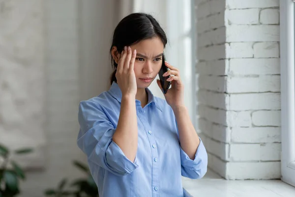 Üzgün Asyalı kadın pencerenin kenarında duruyor, telefonla konuşuyor. — Stok fotoğraf