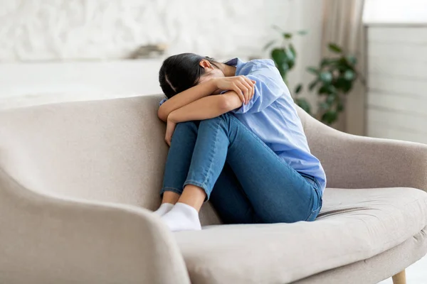 Vista laterale della donna asiatica seduta sul divano, che piange — Foto Stock