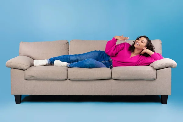 Happy young black woman lying on sofa, feeling hot, waving at herself, mockup for air conditioner or split system design — Φωτογραφία Αρχείου