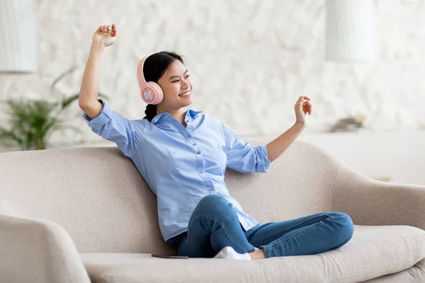 Fröhliche asiatische Frau sitzt auf Couch und hört Musik — Stockfoto