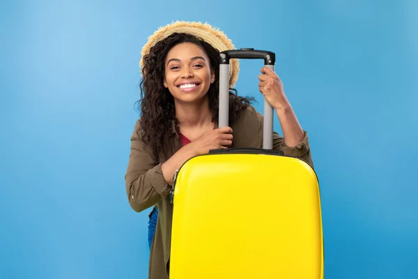 Smiling young African American lady sitting behind bright yellow suitcase, going on summer vacation, having abroad trip — Stockfoto