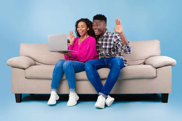 Positivo joven pareja negra que tiene llamada web o chat de vídeo en el ordenador portátil, saludando a la cámara, sentado en el sofá — Foto de Stock