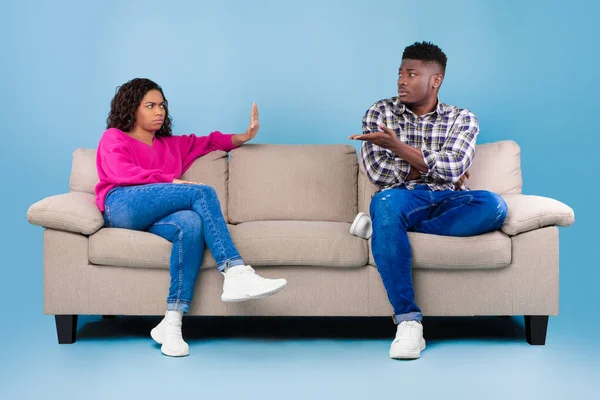 Misunderstanding in relationships. Unhappy young black couple quarrelling on couch over blue studio background — Foto de Stock