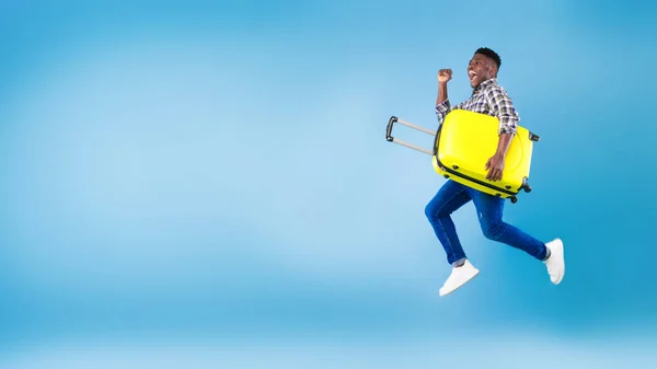 젊은 흑인 남자가 밝은 여행 가방을 들고 점프 , YES 제스처, 파란 배경에서 핫 투어 우승 — 스톡 사진