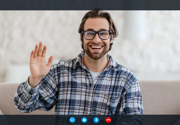 Щасливий молодий білий чоловік зі стерні в окулярах махає рукою, дивитися на веб-камеру в інтер'єрі кімнати на екрані — стокове фото