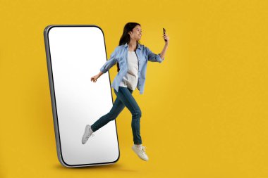 Tatmin olmuş genç Asyalı bayan boş ekranla kocaman bir telefondan atlıyor. Havada donuyor ve akıllı telefona bakın.