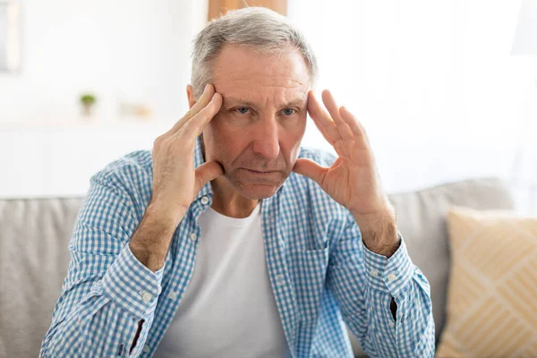 Upset mature man sitting on couch and thinking — ストック写真