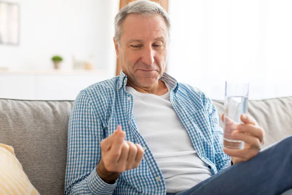 Mature man taking pills holding glass of water — Stock Photo, Image