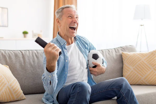 Excitado maduro homem assistindo tv comemorando gol segurando bola — Fotografia de Stock