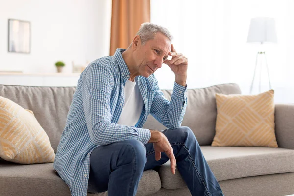 Upset mature man sitting on couch and thinking — Stock Photo, Image