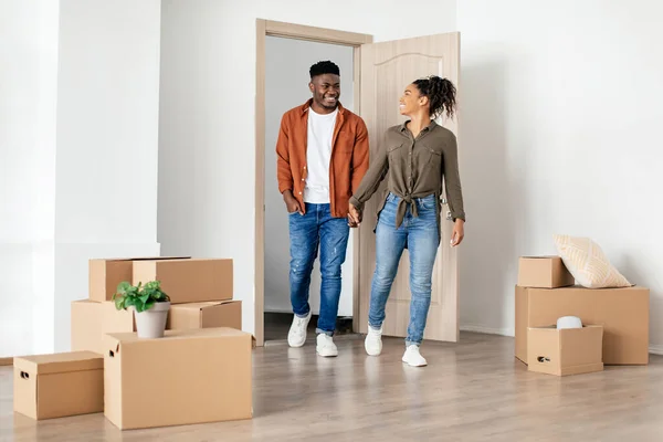 Африканская пара входит в квартиру держа руки глядя на новый дом — стоковое фото