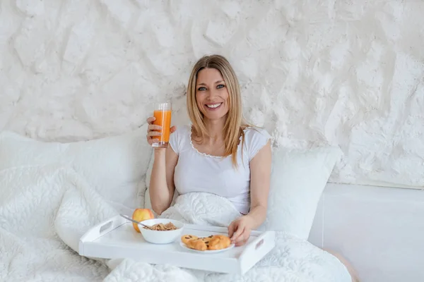 Ικανοποιημένος αρκετά χιλιετή ξανθιά ευρωπαϊκή γυναίκα με ένα ποτήρι χυμό έχουν πρωινό στο κρεβάτι και μόνο — Φωτογραφία Αρχείου