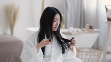 Kırık uçlarına ve kaşlarını çatan yüzüne bakan genç üzgün Asyalı kadın saç şeklinden memnun değil.