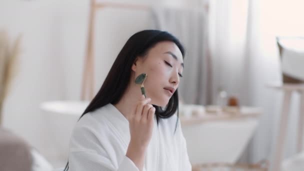 Jovem atraente mulher asiática fazendo auto massagem com massageador de pedra natural, sentado no banheiro em casa — Vídeo de Stock