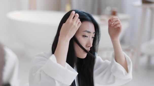 Dandruff problem. Young emotional asian woman wearing bathrobe looking at mirror and examining her dirty hair — Stok video