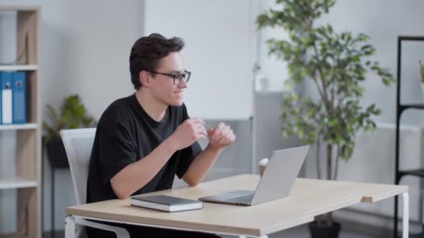 Онлайн-спілкування. Молодий хлопець в окулярах відео балакає з колегами або однокласниками, розмовляє з ноутбуком в офісі — стокове відео