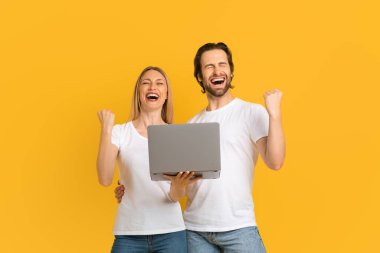 Satisfied excited millennial european couple in white t-shirts rejoice in victory and hold laptop