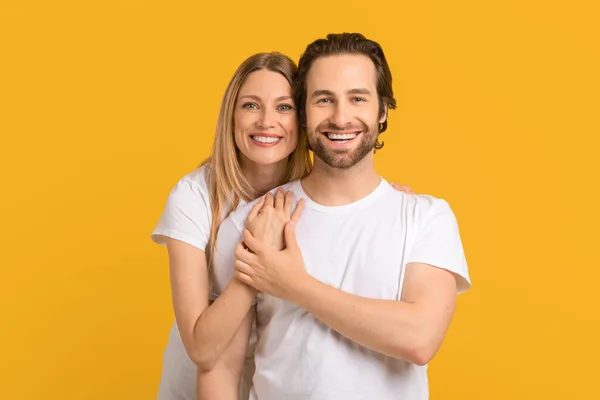Glad smiling young caucasian lady hugging man in white t-shirt looks at copy space —  Fotos de Stock