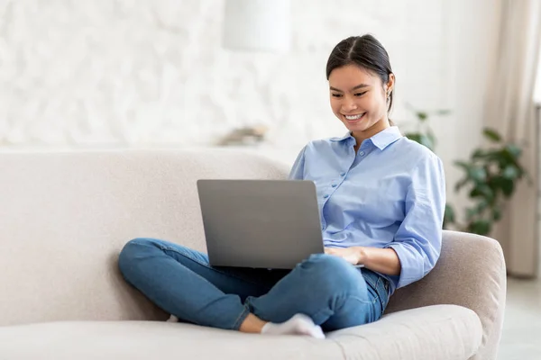 Rilassato asiatico signora seduta su divano, utilizzando laptop — Foto Stock