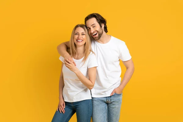 Felice giovane europeo ragazzo e donna in bianco t-shirt abbracci, buon divertimento, isolato su sfondo giallo — Foto Stock