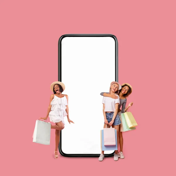 Happy Multiethnic Women Holding Shopping Bags While Posing Near Big Blank Smartphone — Stok fotoğraf