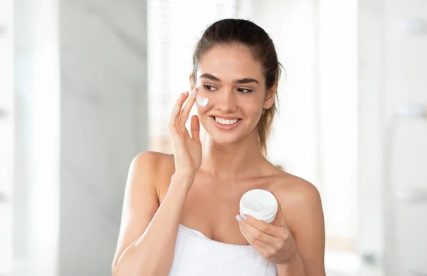 Happy Lady Applying Facial Cream Holding Moisturizer Jar In Bathroom — Fotografia de Stock