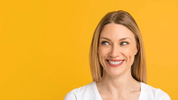 Sonriente alegre joven europea rubia en camiseta blanca mira el espacio libre, aislado sobre fondo amarillo — Foto de Stock