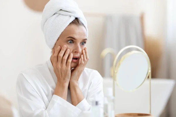 Shocked middle aged woman looking at mirror, touching her skin — Stock fotografie