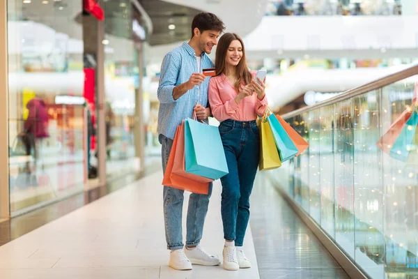 Happy Spouses Shopping Using Smartphone And Credit Card In Mall — Zdjęcie stockowe